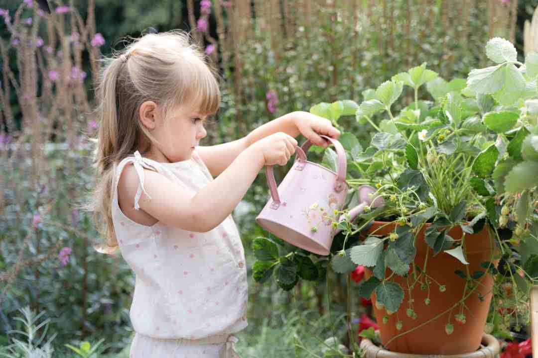 Kind gießt Pflanzen mit einer rosa Kinder Gießkanne im Fairy-Garden-Design – spielerisches Gärtnern fördert Naturverbundenheit und Motorik.