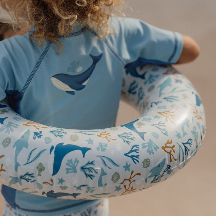 Kind mit Baby-Schwimmring im maritimen Ozean-Design am Pool. Der aufblasbare Schwimmring für Kleinkinder sorgt für unbeschwerten Wasserspaß an warmen Sommertagen und eignet sich ideal für Pool und Urlaub.