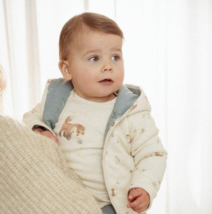 Baby trägt eine weiche Wendejacke in Stone Blue und schaut neugierig zur Seite – stilvolles Baby-Outfit, ideal als Geschenk zur Geburt