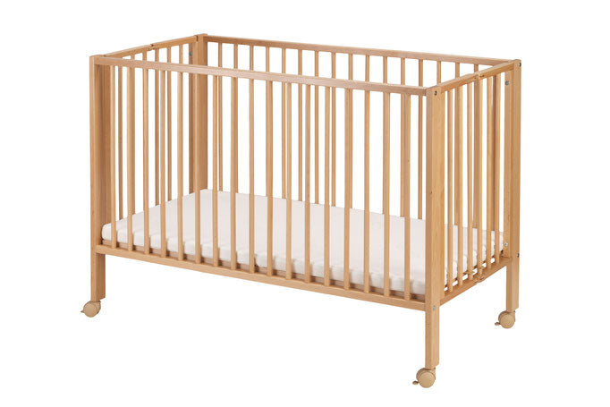 Foldable natural beech wood baby crib with mattress, designed for easy setup and portability on caster wheels.